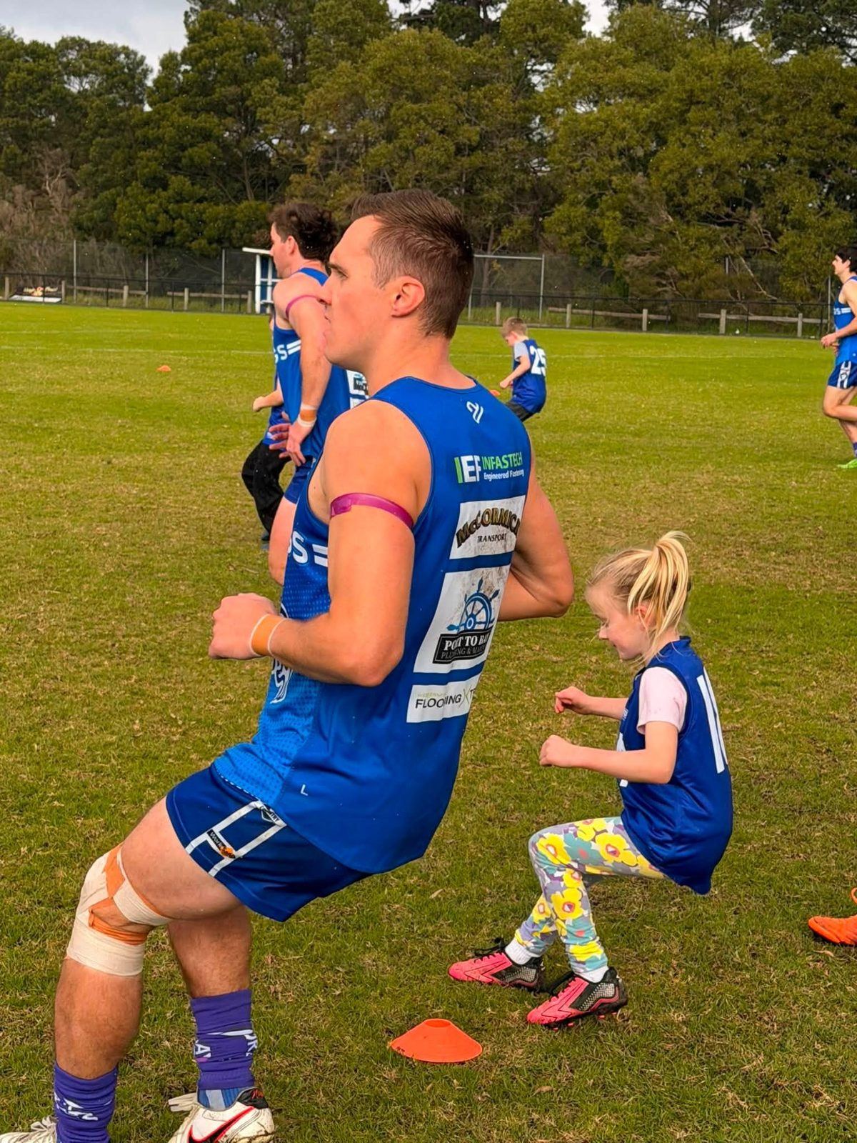 A senior Hastings player runs a drill alongside a young junior on the training track.